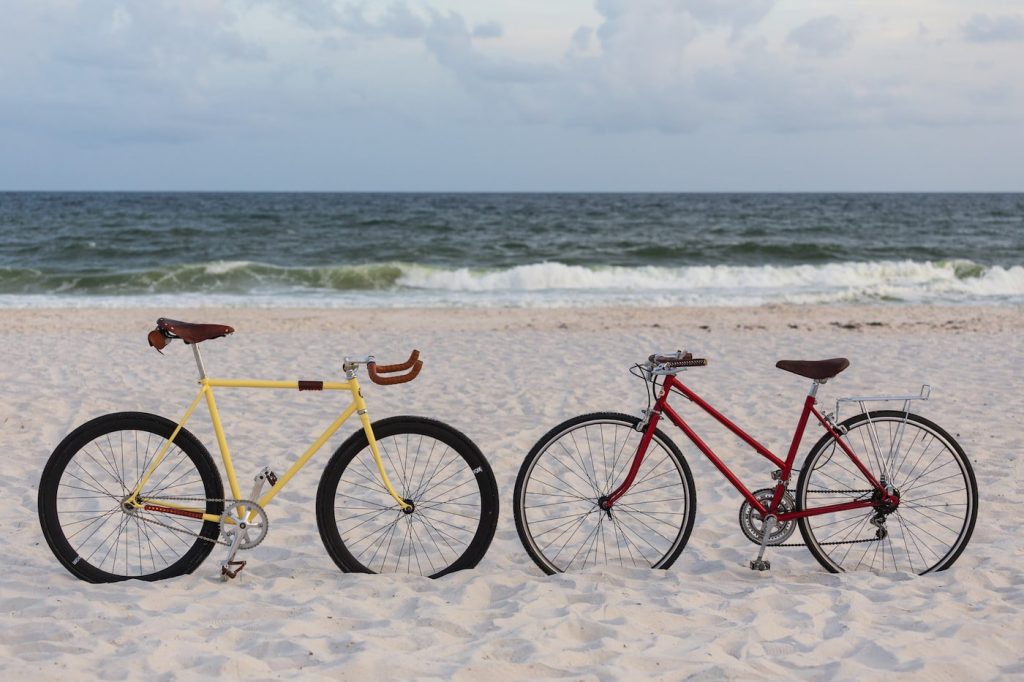 two colorful bikes standing on the beach sand against the sea with an overcast sky